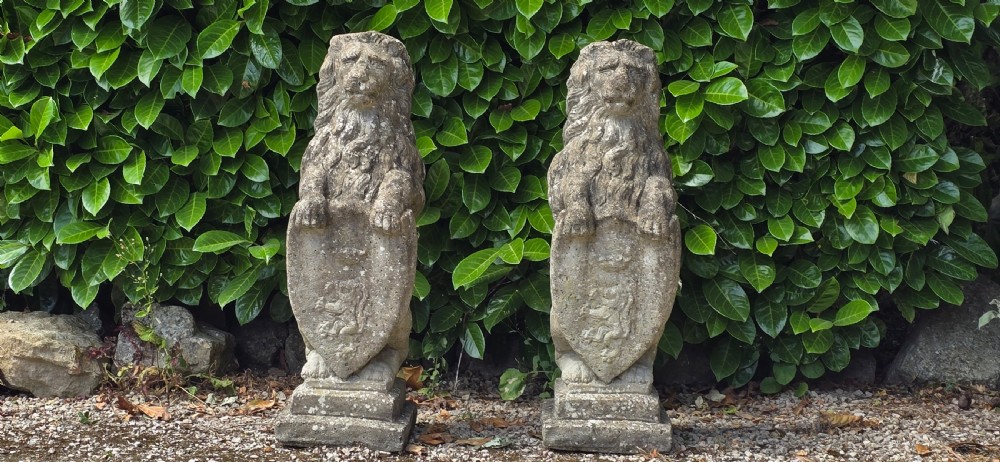 A pair of weathered grey stone garden statues depicting standing lions holding heraldic shields on rectangular bases. View III