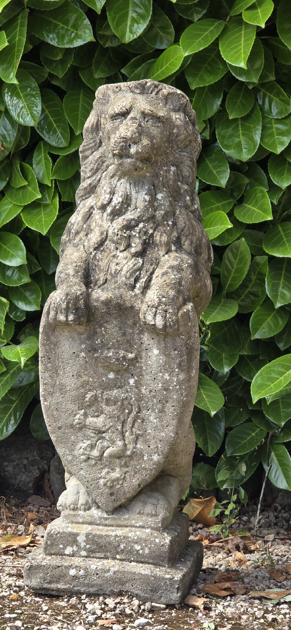A pair of weathered grey stone garden statues depicting standing lions holding heraldic shields on rectangular bases. View V