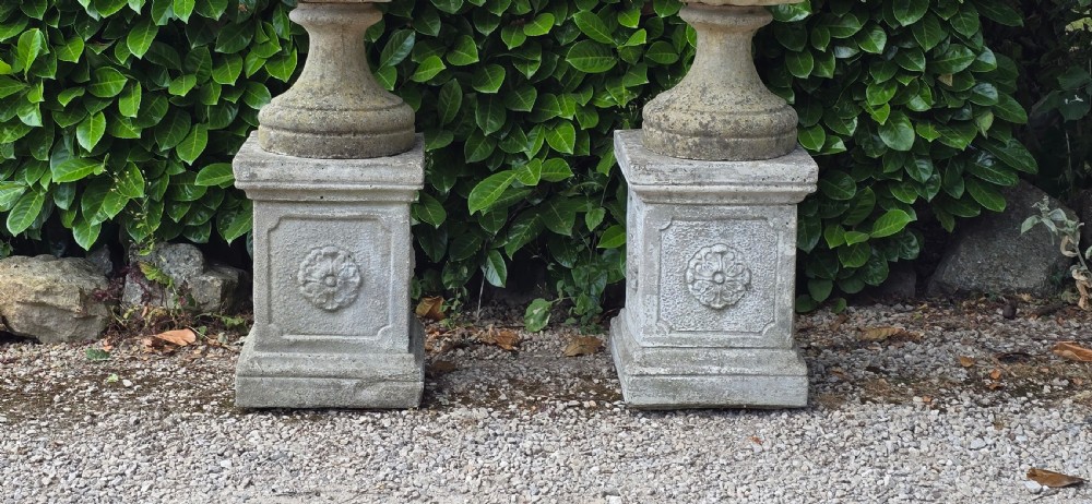 Pair of weathered grey cast stone garden urns featuring fluted bodies and resting on square decorated pedestals. View III