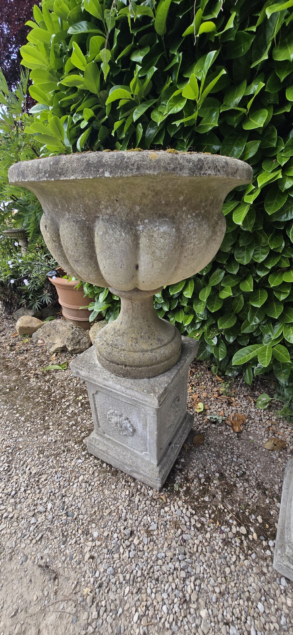 Pair of weathered grey cast stone garden urns featuring fluted bodies and resting on square decorated pedestals. View IV