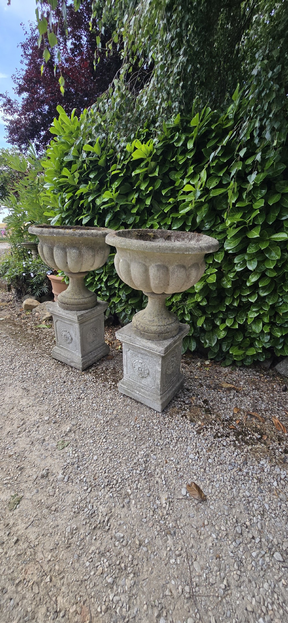 Pair of weathered grey cast stone garden urns featuring fluted bodies and resting on square decorated pedestals. View VII
