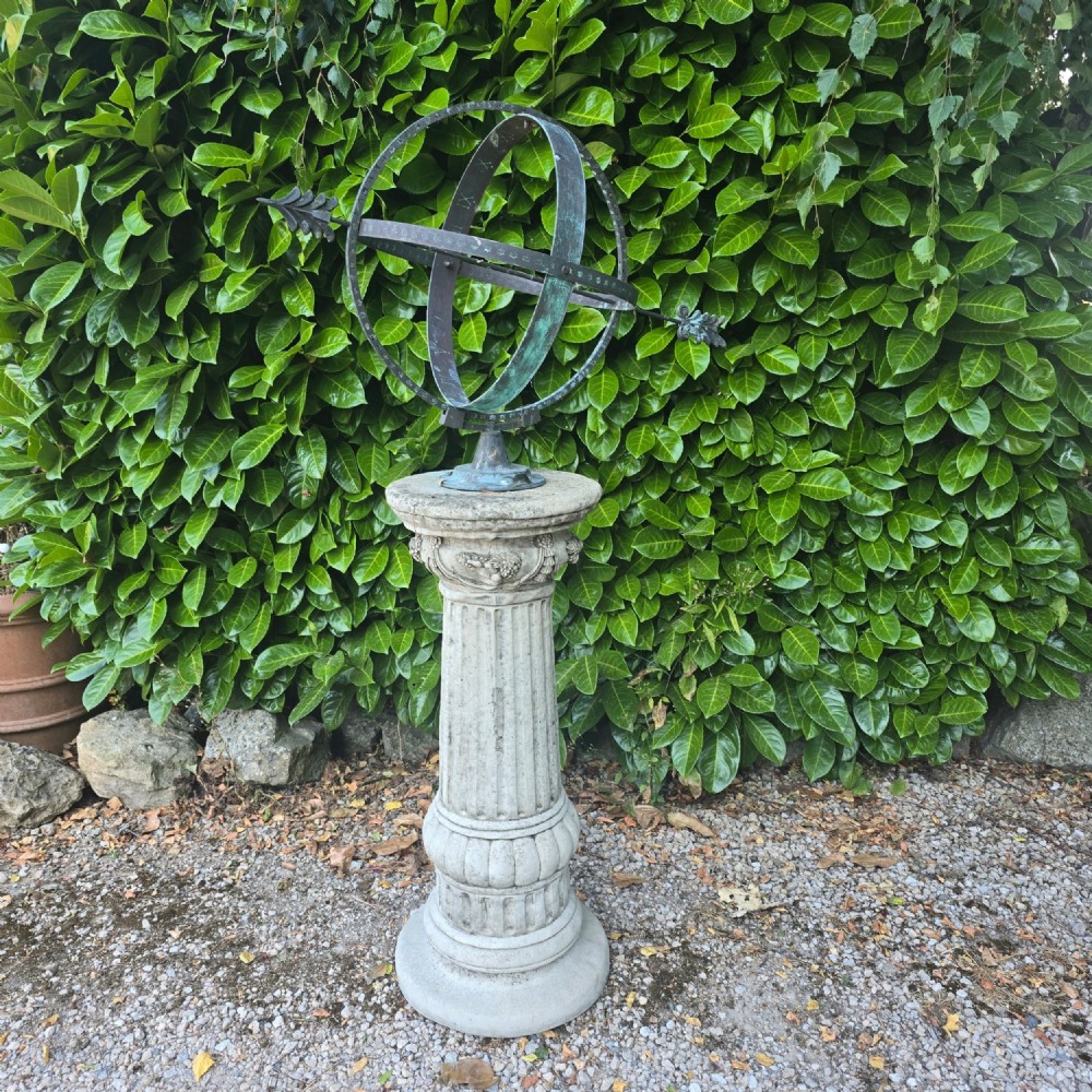A weathered metal armillary sphere with an arrow gnomon and verdigris patina mounted atop a carved fluted stone pedestal.