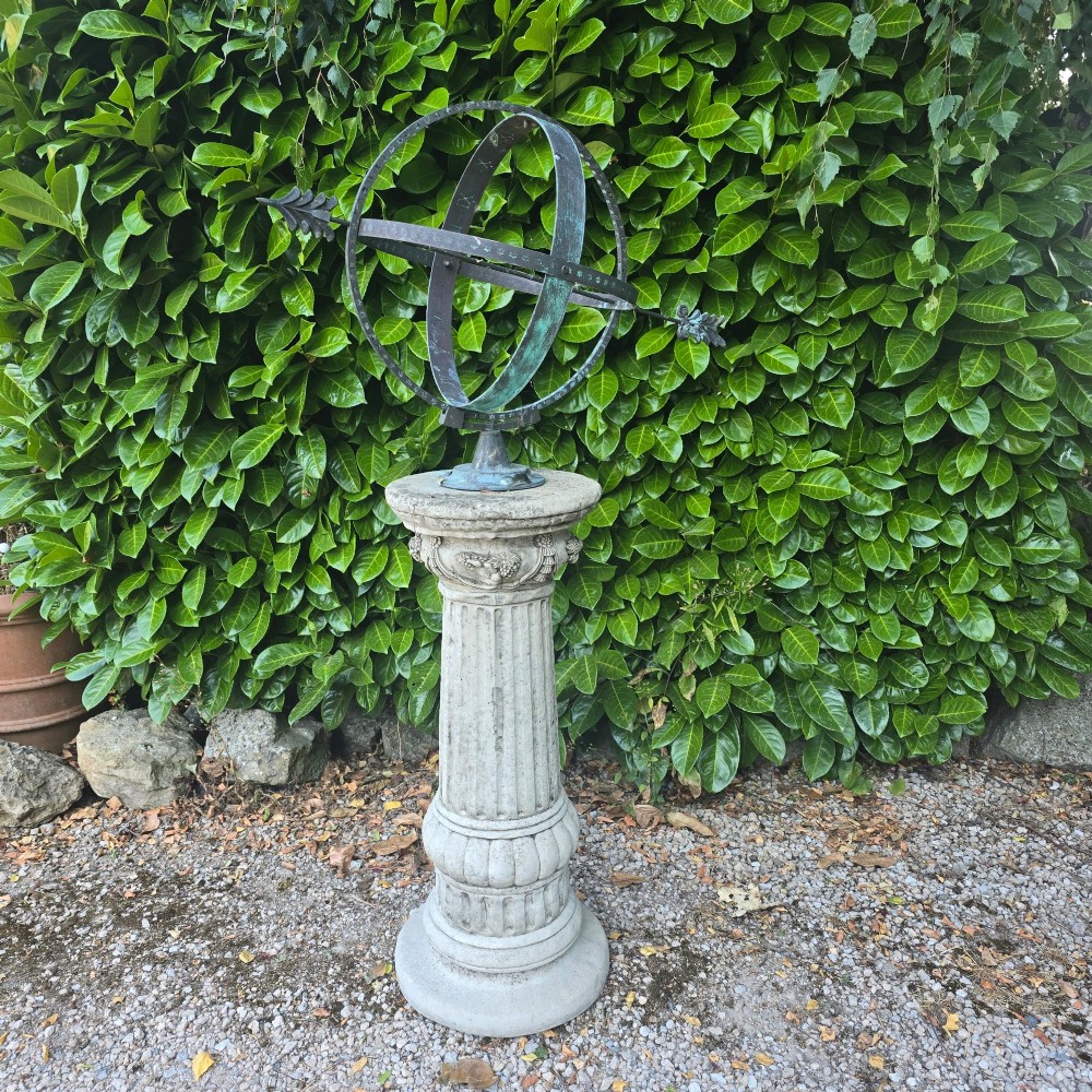 A weathered metal armillary sphere with an arrow gnomon and verdigris patina mounted atop a carved fluted stone pedestal. View II