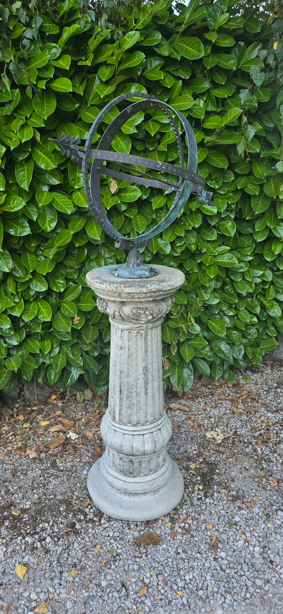 A weathered metal armillary sphere with an arrow gnomon and verdigris patina mounted atop a carved fluted stone pedestal. View III