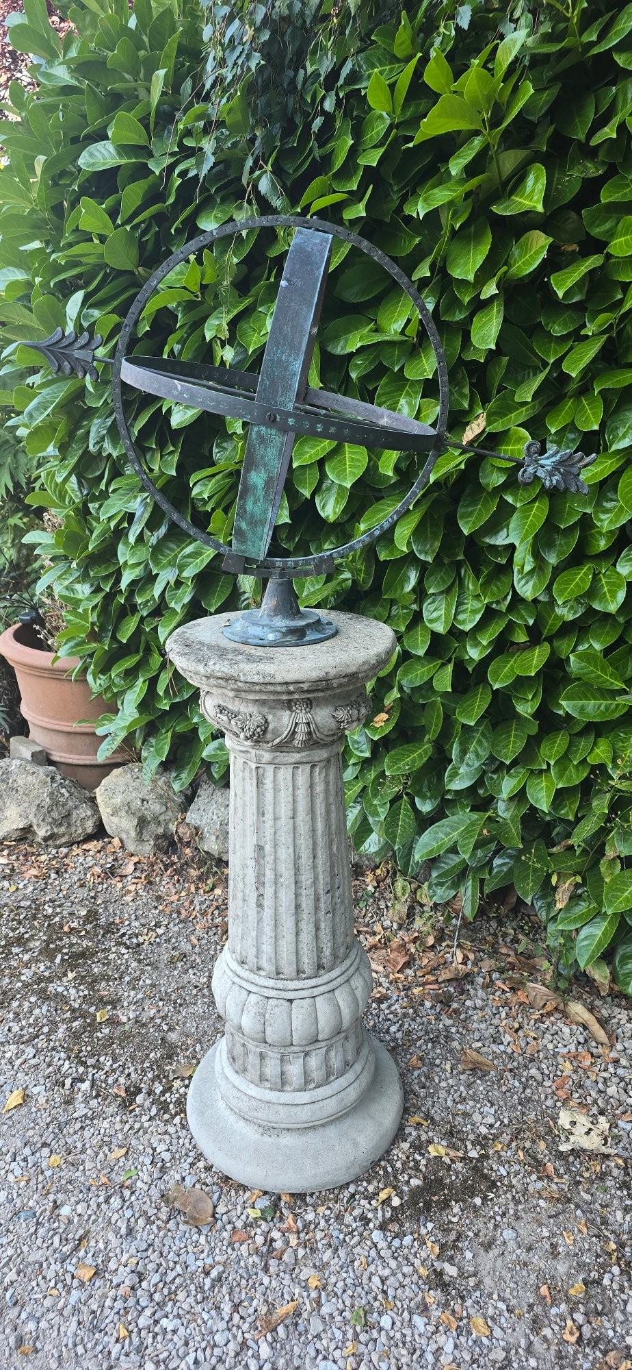 A weathered metal armillary sphere with an arrow gnomon and verdigris patina mounted atop a carved fluted stone pedestal. View IV