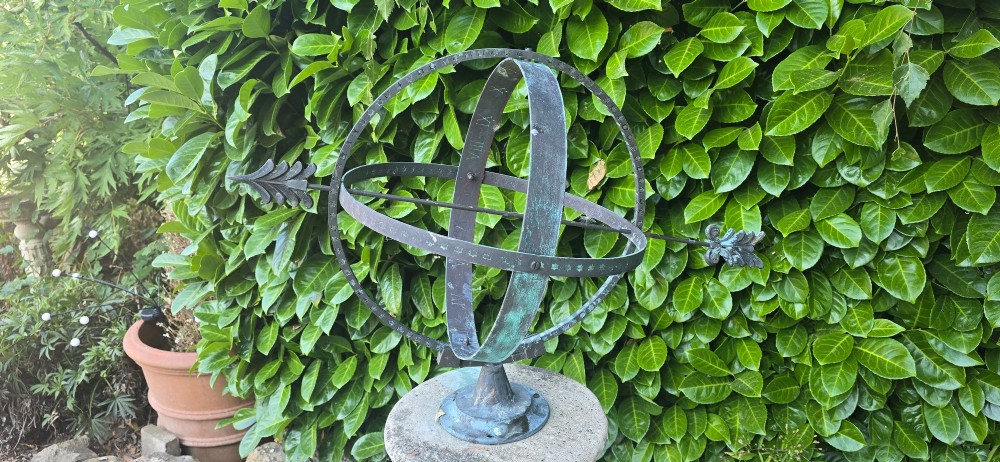 A weathered metal armillary sphere with an arrow gnomon and verdigris patina mounted atop a carved fluted stone pedestal. View VII