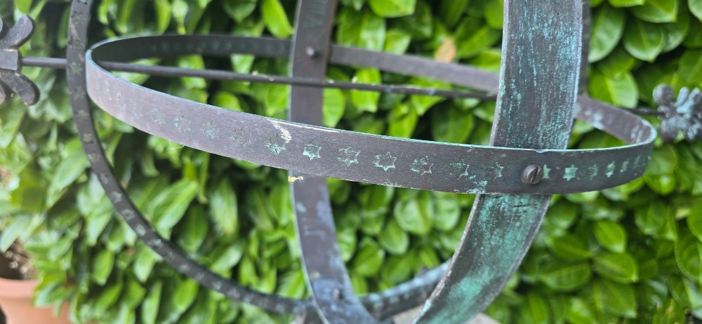 A weathered metal armillary sphere with an arrow gnomon and verdigris patina mounted atop a carved fluted stone pedestal. View VIII