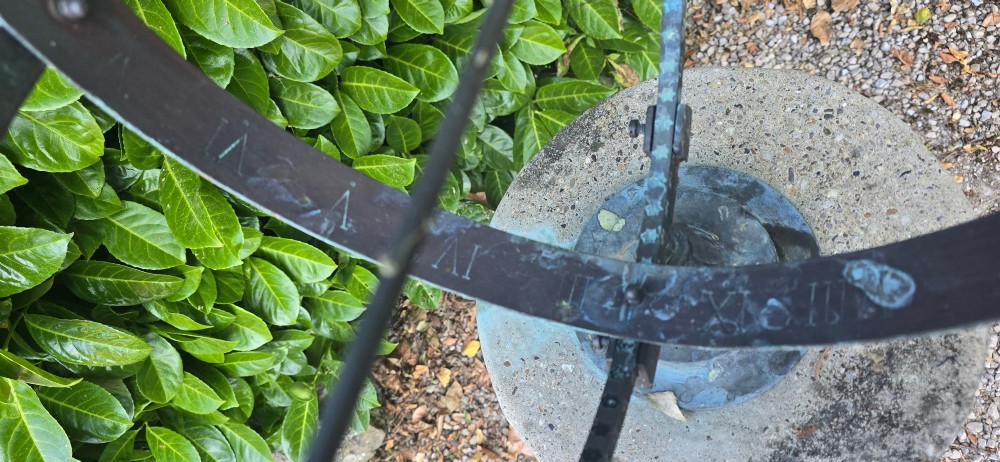 A weathered metal armillary sphere with an arrow gnomon and verdigris patina mounted atop a carved fluted stone pedestal. View XI