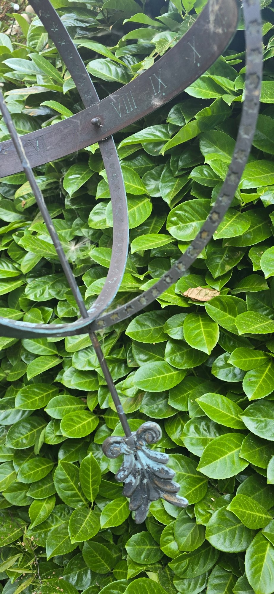 A weathered metal armillary sphere with an arrow gnomon and verdigris patina mounted atop a carved fluted stone pedestal. View XII