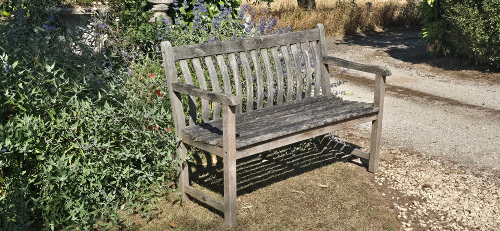 A weathered teak garden bench featuring a vertical slatted backrest, slatted seat, and straight legs connected by stretchers. View IX