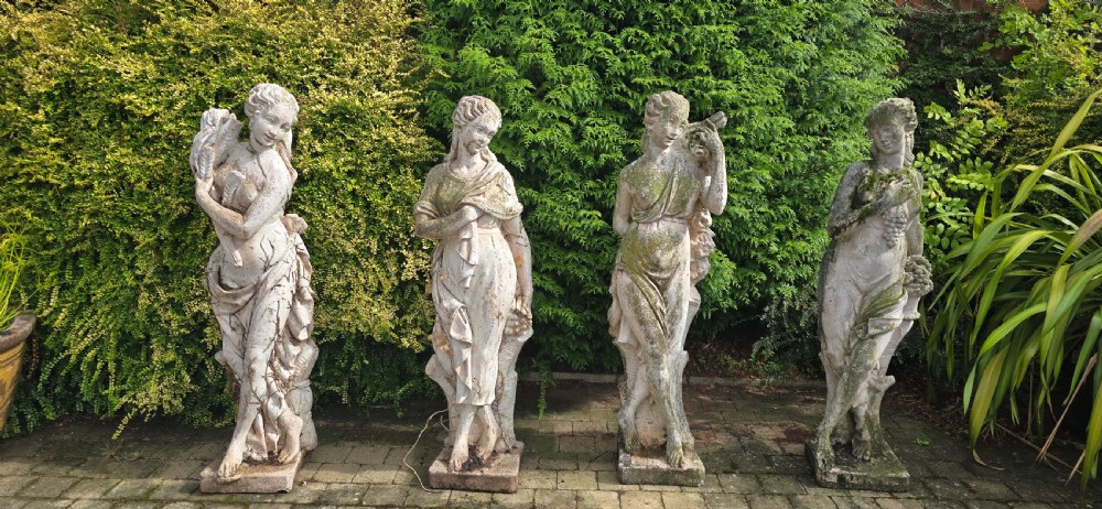 A set of four weathered grey stone full-length classical female statues representing the Four Seasons on rectangular bases. View III