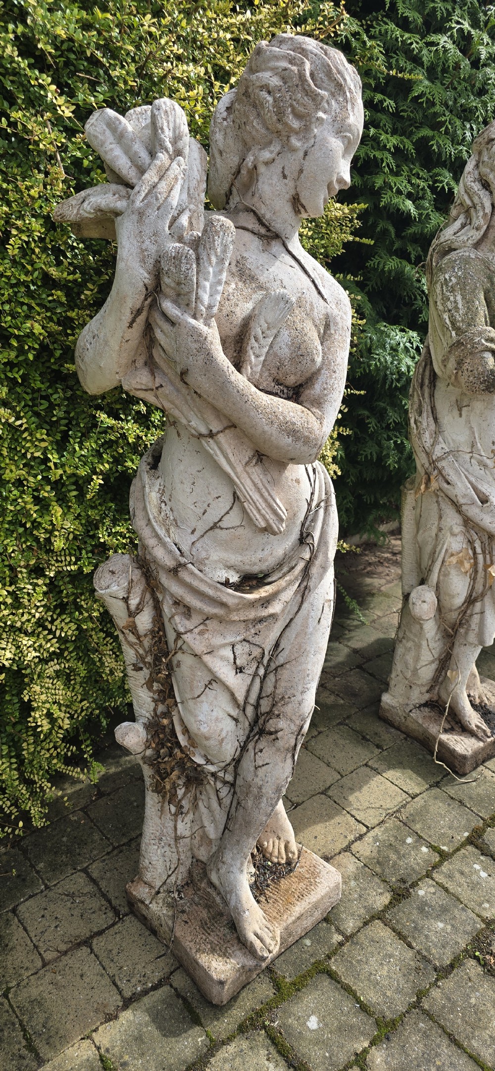 A set of four weathered grey stone full-length classical female statues representing the Four Seasons on rectangular bases. View V