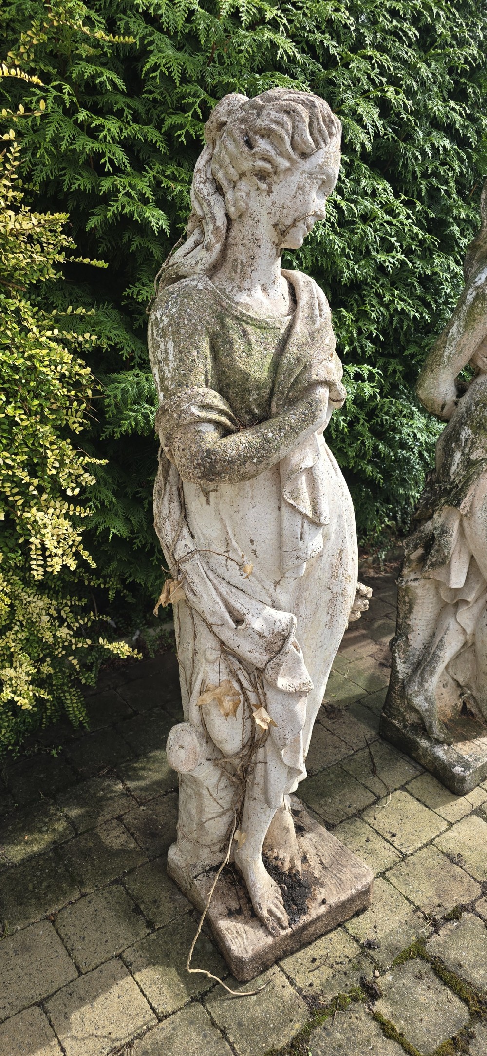 A set of four weathered grey stone full-length classical female statues representing the Four Seasons on rectangular bases. View VI