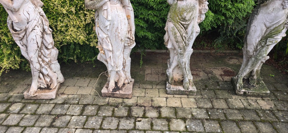 A set of four weathered grey stone full-length classical female statues representing the Four Seasons on rectangular bases. View XII