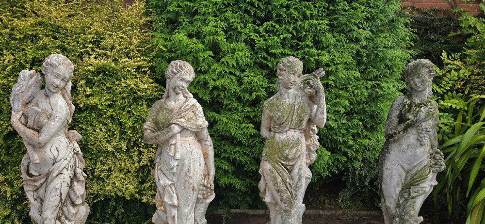 A set of four weathered grey stone full-length classical female statues representing the Four Seasons on rectangular bases. View XIII