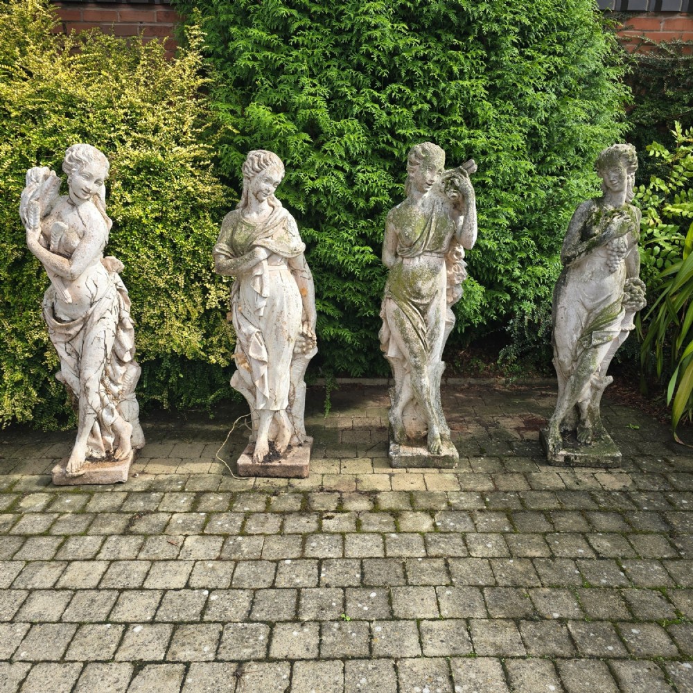 A set of four weathered grey stone full-length classical female statues representing the Four Seasons on rectangular bases.