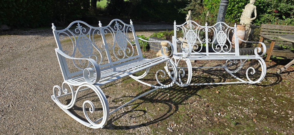 A pair of restored white-painted wrought iron garden rocking benches featuring ornate decorative scrollwork backrests and slatted seats. View IV