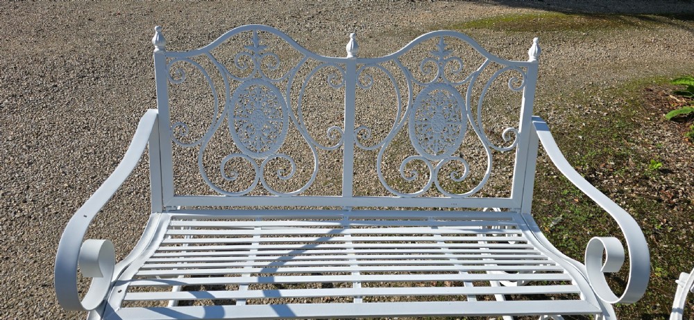 A pair of restored white-painted wrought iron garden rocking benches featuring ornate decorative scrollwork backrests and slatted seats. View VI