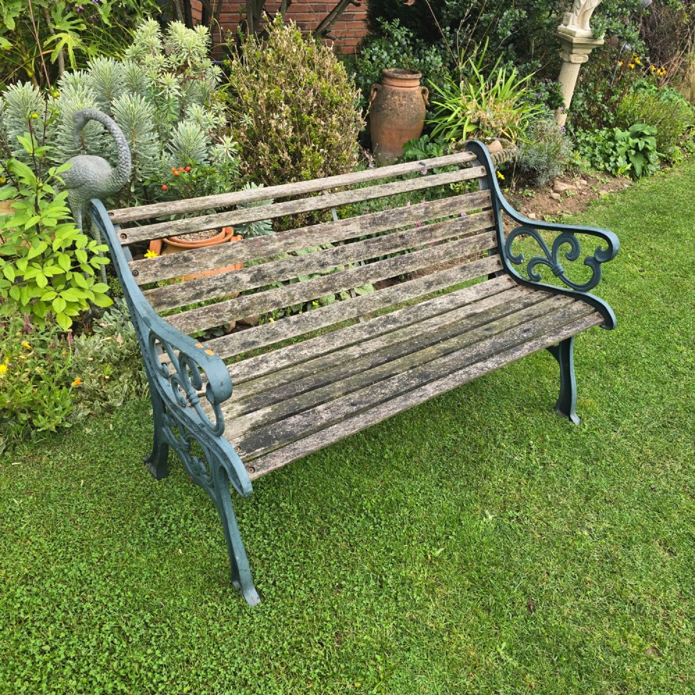 A slatted wooden garden bench with dark green cast iron scrollwork end frames sitting on grass.