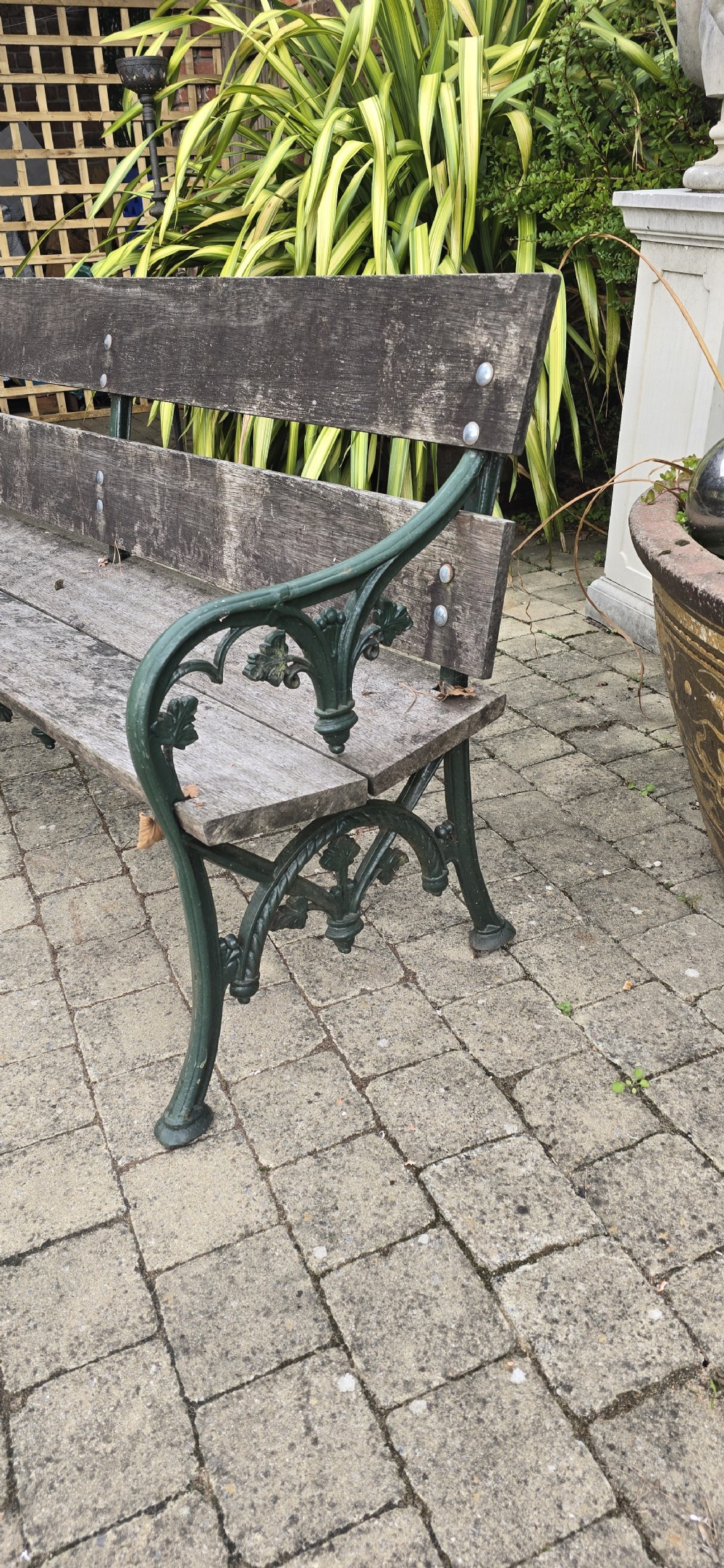 A cast iron garden bench with dark green painted end supports and weathered grey timber slats forming the seat and backrest. View III