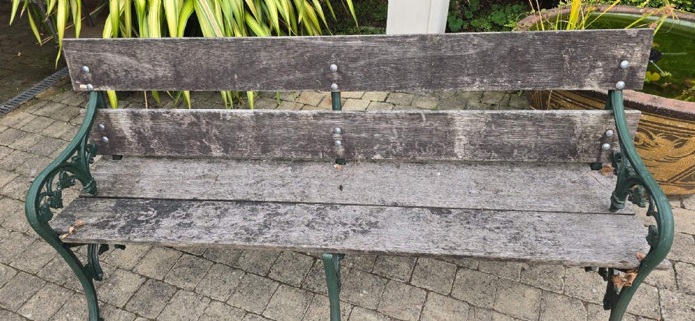 A cast iron garden bench with dark green painted end supports and weathered grey timber slats forming the seat and backrest. View IV
