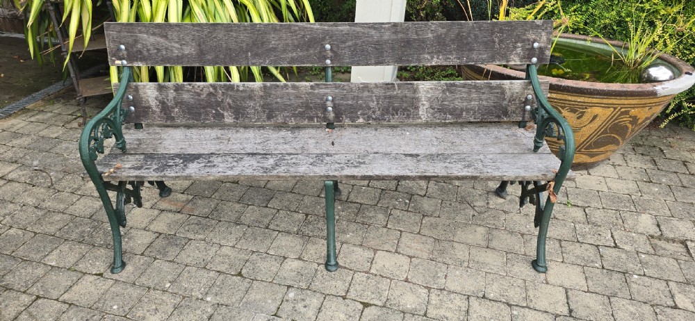 A cast iron garden bench with dark green painted end supports and weathered grey timber slats forming the seat and backrest. View V
