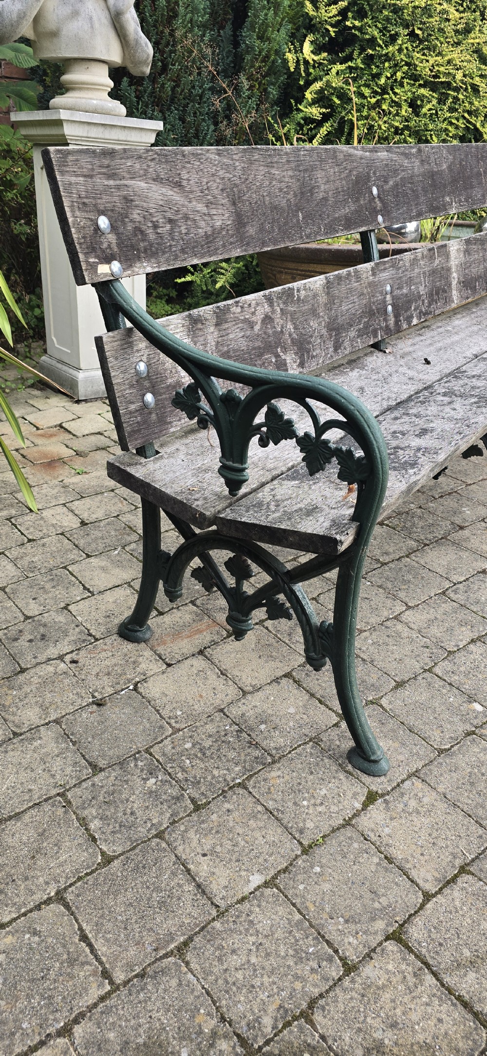 A cast iron garden bench with dark green painted end supports and weathered grey timber slats forming the seat and backrest. View VI
