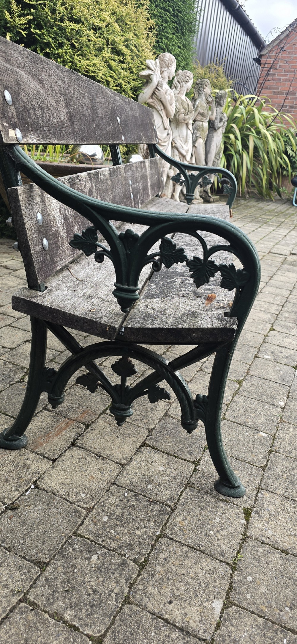 A cast iron garden bench with dark green painted end supports and weathered grey timber slats forming the seat and backrest. View VII