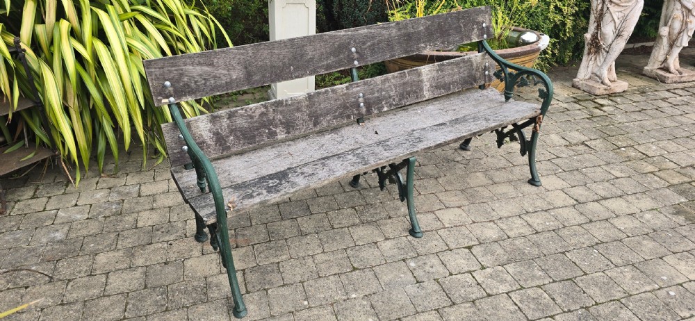 A cast iron garden bench with dark green painted end supports and weathered grey timber slats forming the seat and backrest. View IX