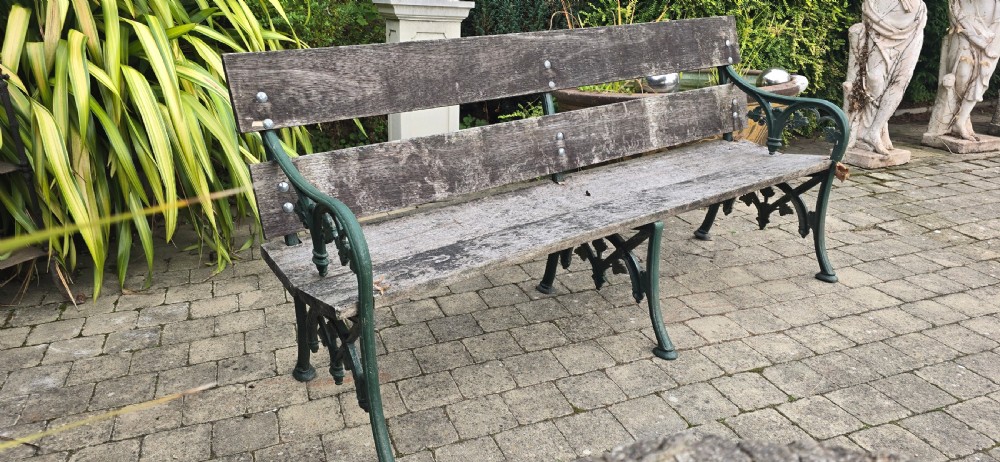 A cast iron garden bench with dark green painted end supports and weathered grey timber slats forming the seat and backrest. View X