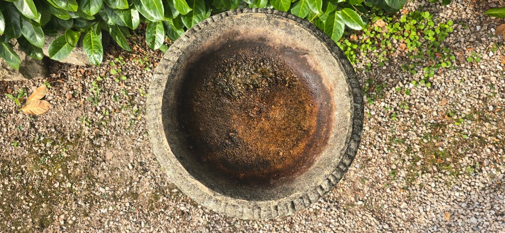 A weathered grey stone bird bath featuring a shallow circular bowl with carved rim detail on a baluster pedestal and round stepped base. View VII