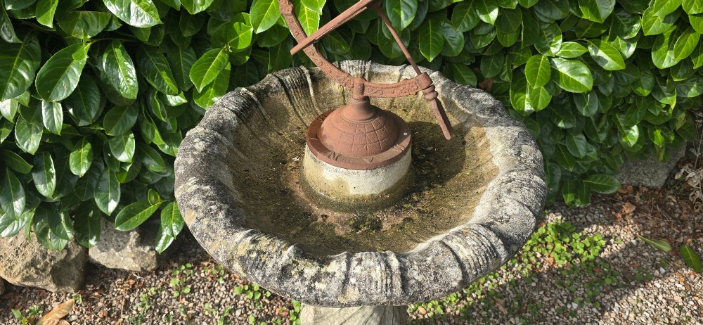 A weathered stone bird bath featuring a spiral-carved pedestal support topped with a rust-brown cast iron armillary sphere. View III
