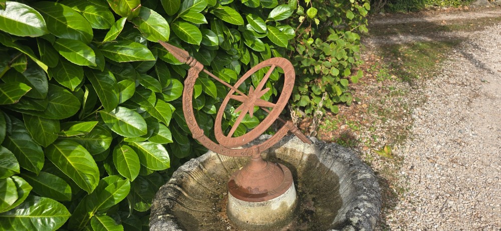 A weathered stone bird bath featuring a spiral-carved pedestal support topped with a rust-brown cast iron armillary sphere. View IV