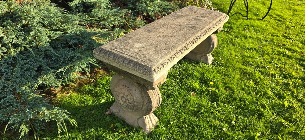 A rectangular weathered stone garden bench featuring carved scroll supports set on lawn grass. View IV