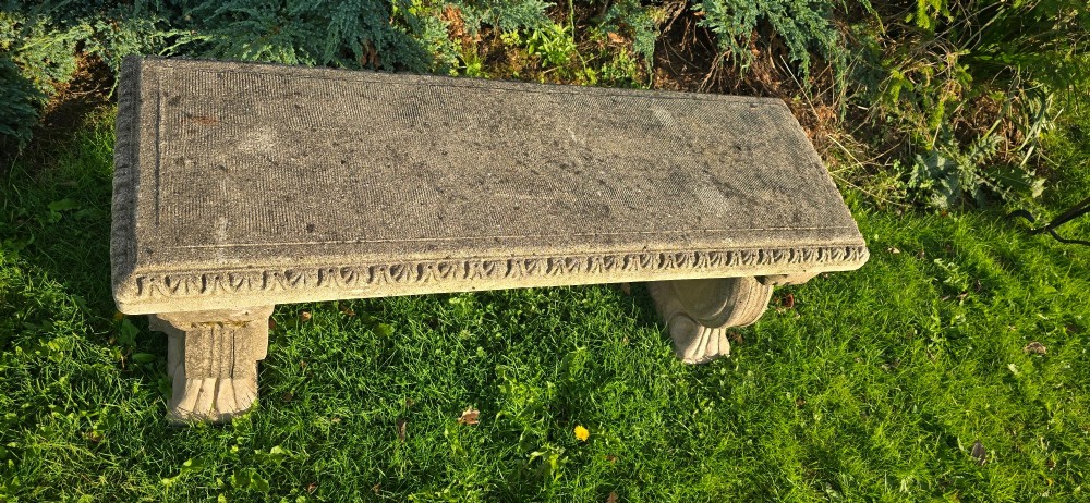 A rectangular weathered stone garden bench featuring carved scroll supports set on lawn grass. View V