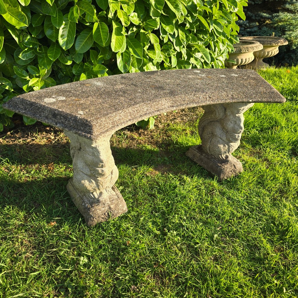 A curved weathered grey stone garden bench featuring a bevelled seat resting on two sculpted animal-form pedestal supports. View III
