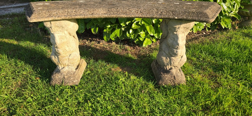 A curved weathered grey stone garden bench featuring a bevelled seat resting on two sculpted animal-form pedestal supports. View V