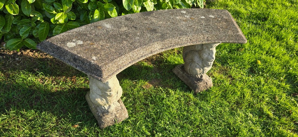 A curved weathered grey stone garden bench featuring a bevelled seat resting on two sculpted animal-form pedestal supports. View VIII