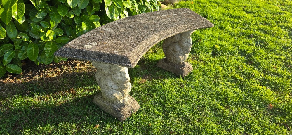 A curved weathered grey stone garden bench featuring a bevelled seat resting on two sculpted animal-form pedestal supports. View IX