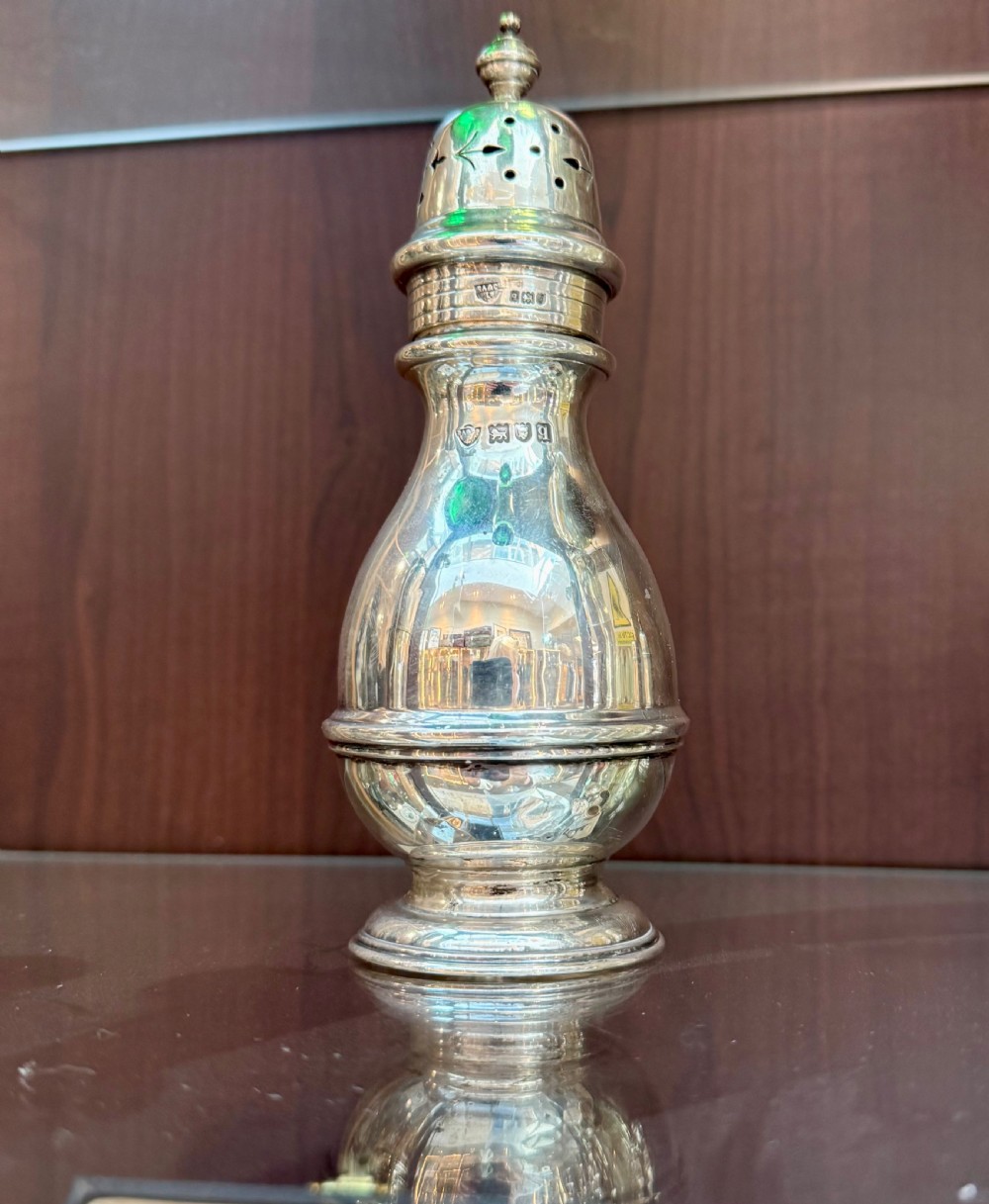A hallmarked sterling silver sugar caster featuring a baluster form, pierced dome lid with finial, and moulded pedestal base.