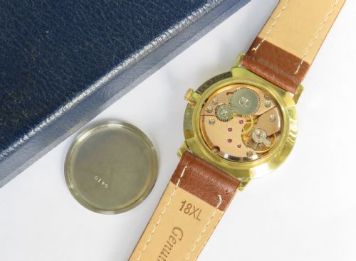 fig 2. A 1960s gents Garrard wristwatch with a gold-toned case, off-white dial, baton markers, and brown leather strap resting inside a navy blue velvet presentation box.