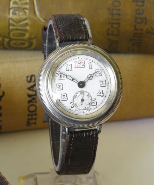 fig 1. A 1930s gentlemans silver hermetic wrist watch with a circular coin-edge bezel, white enamel dial, sub-seconds display, and brown leather strap.