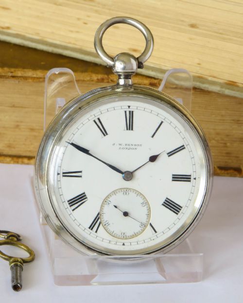 fig 1. An open-face silver pocket watch with a white enamel dial, black Roman numerals, blued steel hands, and a separate winding key.