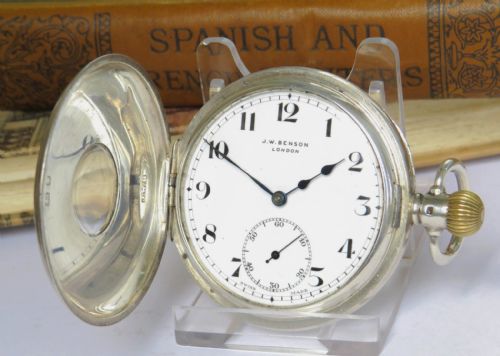 fig 1. An antique silver half-hunter pocket watch featuring an outer enamel chapter ring with Roman numerals around a central circular glass window.