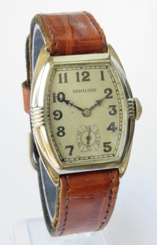 fig 1. A 1930s Art Deco gents Hamilton wristwatch with a gold-toned tonneau case, cream dial, Arabic numerals, sub-seconds dial, and brown leather strap.