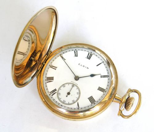 fig 1. An open gold-toned full hunter pocket watch displaying a white enamel dial with black Roman numerals and a small seconds dial.