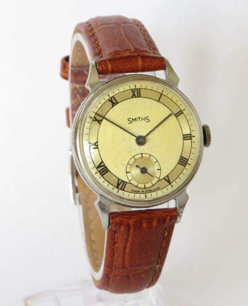 fig 1. A mid-20th-century gents Smiths wristwatch featuring a champagne dial with Roman numerals, subsidiary seconds dial, silver-tone case, and tan leather strap.