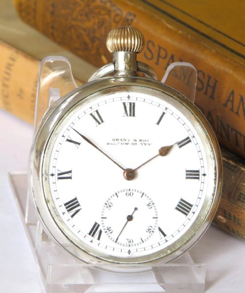 fig 1. An antique open-face silver pocket watch featuring a white enamel dial with black Roman numerals and a small seconds sub-dial at six oclock.