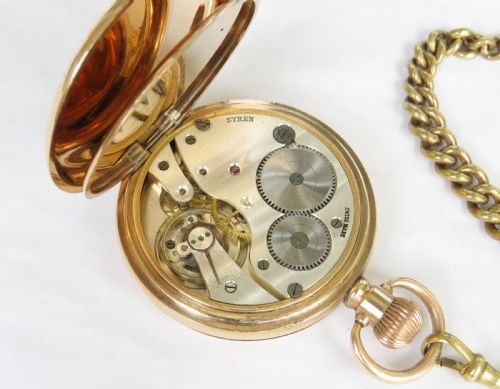 fig 2. An antique 1920s gold-plated open-face pocket watch by Syren featuring a white enamel dial with Roman numerals, a sub-seconds dial, and an attached curb link chain with a tassel fob.
