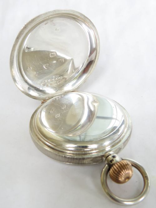 fig 2. A silver full hunter pocket watch shown open to display a white enamel dial with black Roman numerals and a small seconds sub-dial.